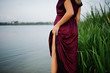 © AS Photo Family - Blonde sensual woman in red marsala dress standing in water of lake with reeds and show her nude leg.