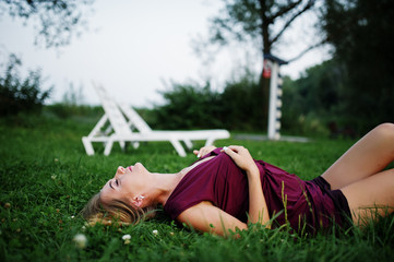 Wall Mural - Blonde sensual woman in red marsala dress lying in the green grass.