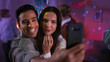 © Gorodenkoff - At the Wild House Party: Beautiful Young Couple Take Selfies with a Smartphone for Social Network Sharing. In the Background Crowd of Young People Dancing Off and Having Fun.