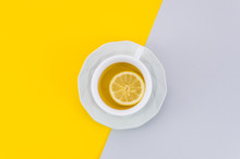 An Overhead View Of Lemon Tea Cup And Saucer On White And Yellow Background