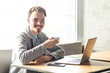 © khosrork - Portrait of handsome happy bearded young businessman in grey blazer are sitting in cafe and have a break with cup of coffee and toothy smile are looking at camera. Indoor, freelancer lifestyle