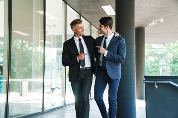 Portrait of two smiling businessmen partners walking outside job center during working meeting