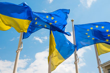 Row Of Flagpoles With European Union And Ukraine Flags Fluttering By Wind On Blue Sky Background