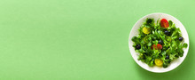 Banner Of Fresh Salad Of Arugula And Valerian Leaves With Colored Tomatoes And Blueberries In A Plate On A Green Background.