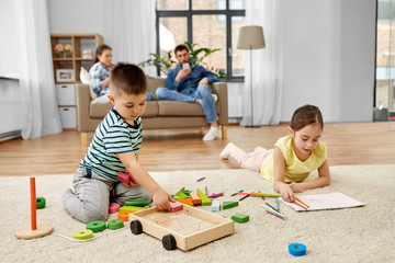 childhood, leisure and family concept - brother playing toy blocks and sister drawing by crayons at home