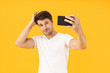 Man in casual white t-shirt take a selfie by mobile phone isolated over yellow background.