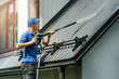© ronstik - man standing on ladder and cleaning house metal roof with high pressure washer