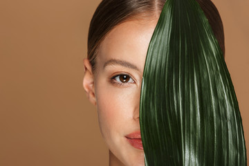 Canvas Print - Image of calm half-naked woman looking at camera and covering her face with green leaf