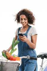 Poster - Image of happy african american woman with shopping bag holding cellphone while riding bicycle