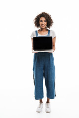 Wall Mural - Image of brunette african american woman dressed in denim overalls smiling and holding open laptop