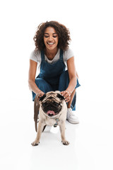 Poster - Image of happy african american woman dressed in denim overalls squatting and poising with her pug dog