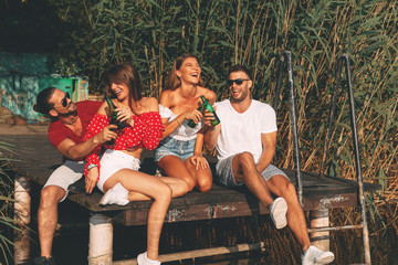 Sticker - Happy group of young people drinking beer on a dock by the river during the summer sunny day