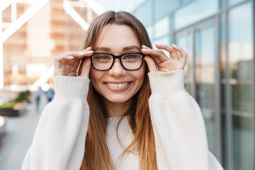 Poster - Beautiful young happy excited business woman posing walking outdoors near business center wearing eyeglasses.