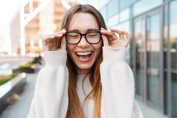 Poster - Beautiful young happy excited business woman posing walking outdoors near business center wearing eyeglasses.