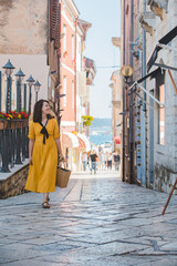 Wall Mural - young pretty woman in yellow dress walking by small porec city streets sea on background