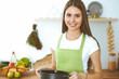 © rogerphoto - Young happy woman cooking soup in the kitchen. Healthy meal, lifestyle and culinary concept. Smiling student girl preparing vegetarian meal at home
