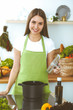 © rogerphoto - Young happy woman cooking soup in the kitchen. Healthy meal, lifestyle and culinary concept. Smiling student girl preparing vegetarian meal at home