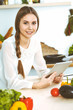 © rogerphoto - Young woman using tablet while cooking or making online shopping in kitchen. Girl looking at the camera. Healthy lifestyle and vegan meal concepts