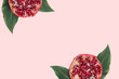 Red slices pomegranate with green leaves on the pink minimal background. Exotic fruit flatlay with copyspace