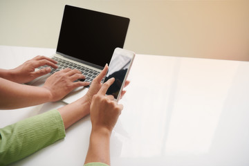 an asian man and a woman are searching information on the .nternet on laptop computer and the mobile phone for online shopping on the white table.