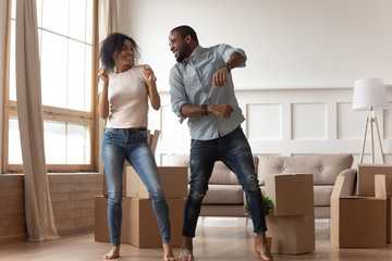 Wall Mural - Happy african couple dancing laughing in living room with boxes