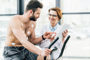 smiling doctor with digital tablet near shirtless sportsman during endurance test