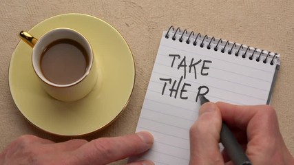 Canvas Print - take the risk - a man hand writing a note with a black marker in a notebook, overhead view with a cu