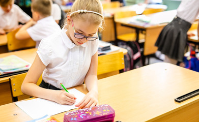 Blonde girl with big glasses sitting in classroom, studing, smiling. Education on elementary school, first day at school