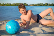 A Teenager Lying On The Beach With A Ball On A Sunny Day Against The Background Of The River, A Close-up.