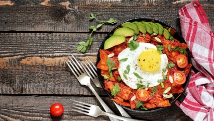 Sticker - mexican breakfast Chilaquiles . tortilla chips are lightly stewed in a red tomato and paprika chili sauce, scrambled eggs are added and served in a pan with avocado and green onions and cilantro. 