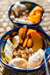 Macro closeup of two bowls of granola cereal dish made from oats with fresh sliced banana fruit and peaches nectarines romantic healthy breakfast