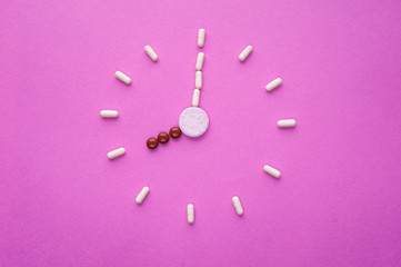 Wall Mural - Clock created from white pills and brown tablets on pink background. Right time for using medicines. Brown and white capsules is eight o'clock. Concept: medicine, drugs, healthcare, painkillers, time.