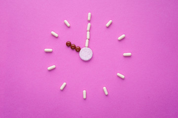 Wall Mural - Clock created from white pills and brown tablets on pink background. Right time for using medicines. Brown and white capsules is ten o'clock. Concept: medicine, drugs, healthcare, painkillers, time.