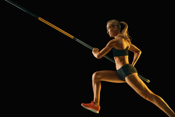 Power and beauty. Professional female pole vaulter training on black studio background in neon light. Fit female model practicing. Concept of sport, healthy lifestyle, action, movement, motion.