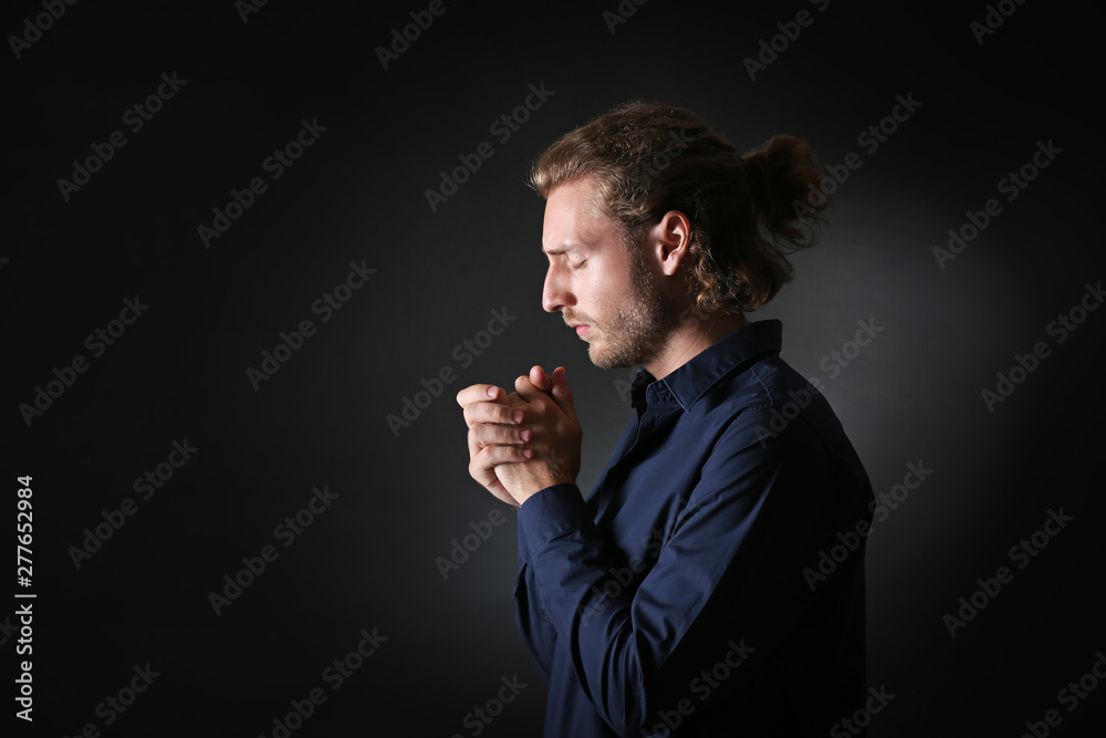 Religious young man praying on dark background
