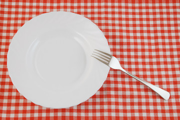 Top view of white plate and fork on tablecloth