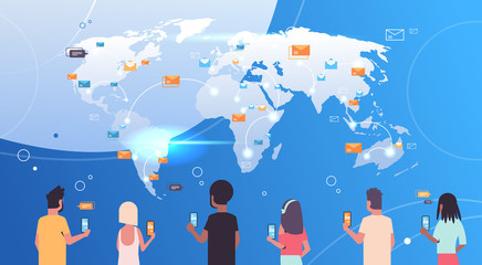 Poster - rear view people using mobile messenger application men women holding smartphones sending email envelope letter global communication concept world map background flat portrait horizontal