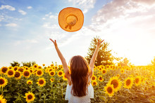Young Woman Walking In Blooming Sunflower Field Throwing Hat Up And Having Fun. Summer Vacation
