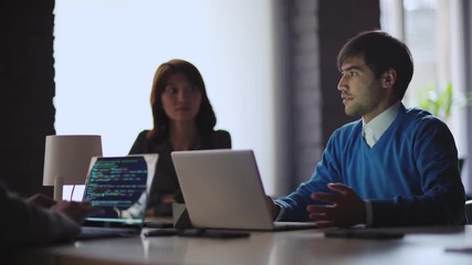 Team of four young business people planning online startup at meeting. Focus on smiling Middle Eastern man explaining his ideas. Female programmer coding on laptop, tracking shot