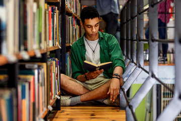 Wall Mural - Young male student study in the library reading book while sitting near bookshelf.