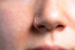 A closeup view on the pierced nose of a beautiful Caucasian woman. Front view showing details of a small silver nose-ring piercing the alae.