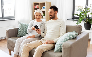 family, generation and people concept - happy smiling senior mother and adult son with smartphone networking at home