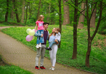 Wall Mural - Happy young family with their two children are walking in summer forest park, parenthood vacations with kids