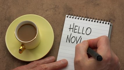 Canvas Print - hello november - a man hand writing a note with a black marker in a notebook, overhead view with a c