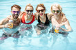 Portrait of a group of happy friends standing together in the swimming pool, having fun drinking juice and enjoying the summer time
