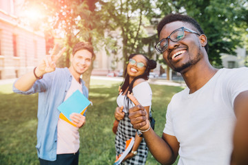 Education,leisure and technology concept. Cheerful friends from different countries and races taking selfie with back lighting. Happy youth people having fun in university campus. Sun glare effect.