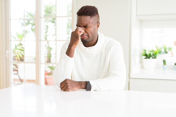 Wall Mural - Handsome african american man on white table smelling something stinky and disgusting, intolerable smell, holding breath with fingers on nose. Bad smells concept.