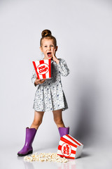 Wall Mural - Portrait of a cheery pretty girl holding plastic cup and eating popcorn isolated over white background