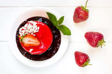 Juicy tasty bright red strawberry cake on a white wooden background, decorated with fresh strawberries and beautiful green mint leaves