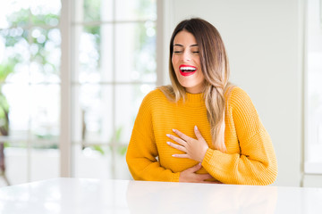 Wall Mural - Young beautiful woman wearing winter sweater at home Smiling and laughing hard out loud because funny crazy joke. Happy expression.